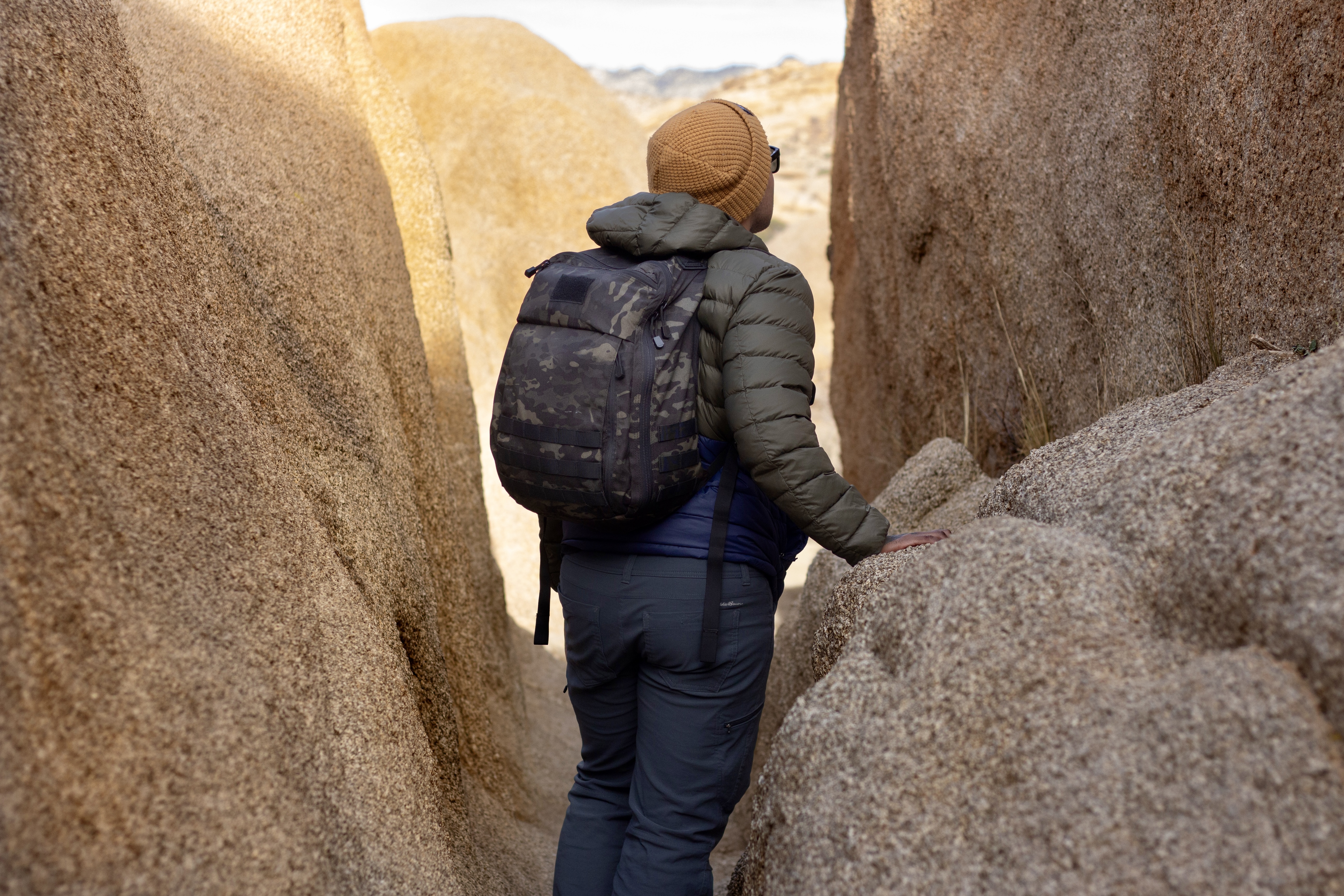 image of a person in between two large boulders wearing the prime pack in multicam black